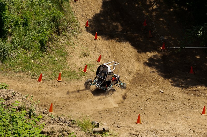 Baja car descending a steep dirt slope lined with orange cones