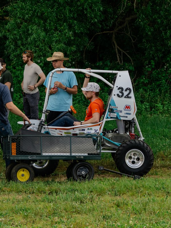 Team moving Baja car number 32 on a wheeled cart across the grass
