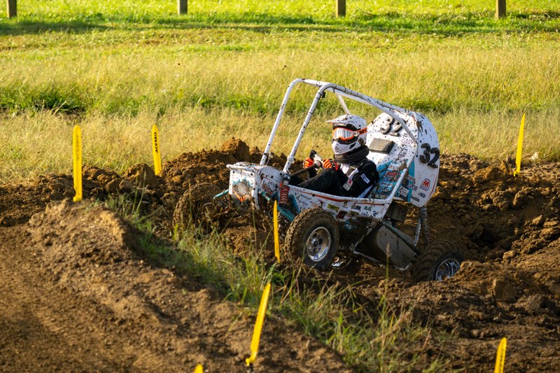 Baja car number 32 climbing out of a deep rut between marker stakes