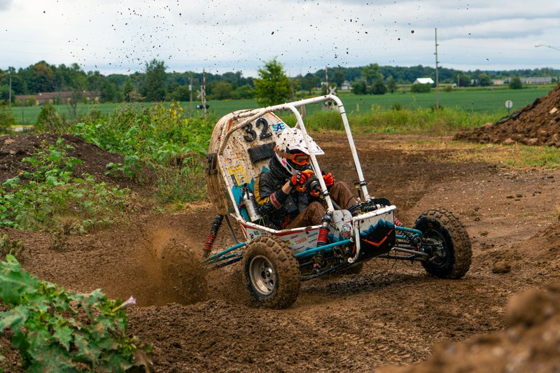 Baja car number 32 turning hard across a muddy field, tires throwing dirt
