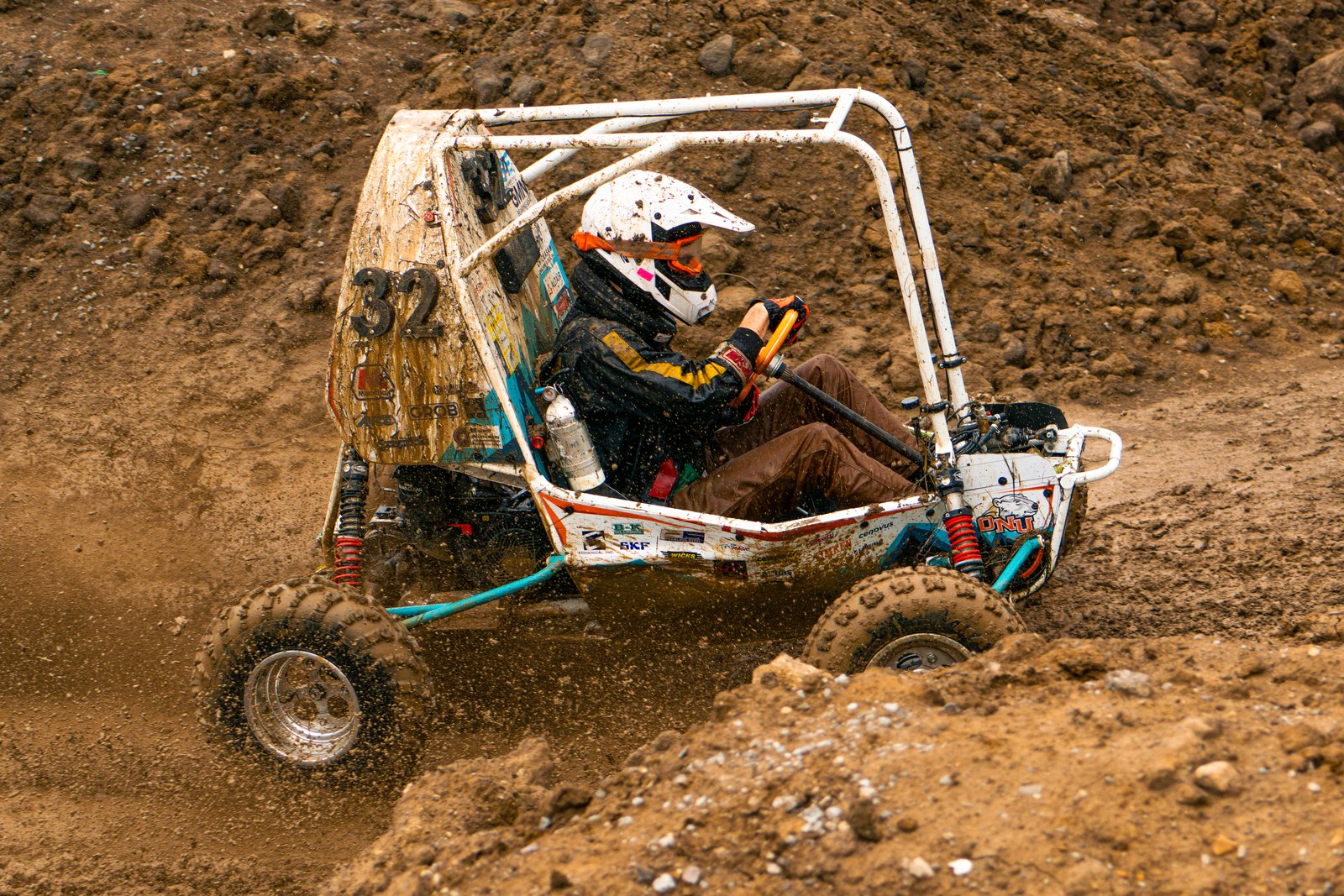 Baja car number 32 driving hard through loose dirt, front suspension compressed and dirt spraying from the tires