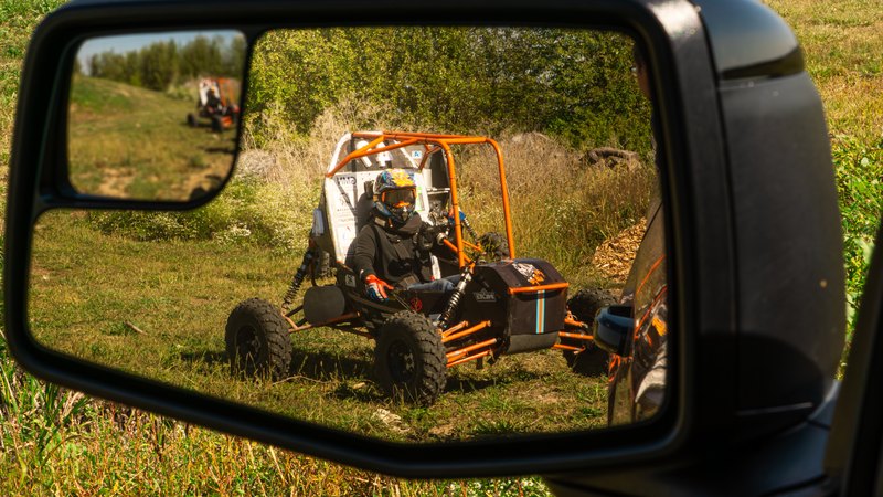 Baja car number 49 seen in a truck side mirror on a dirt course