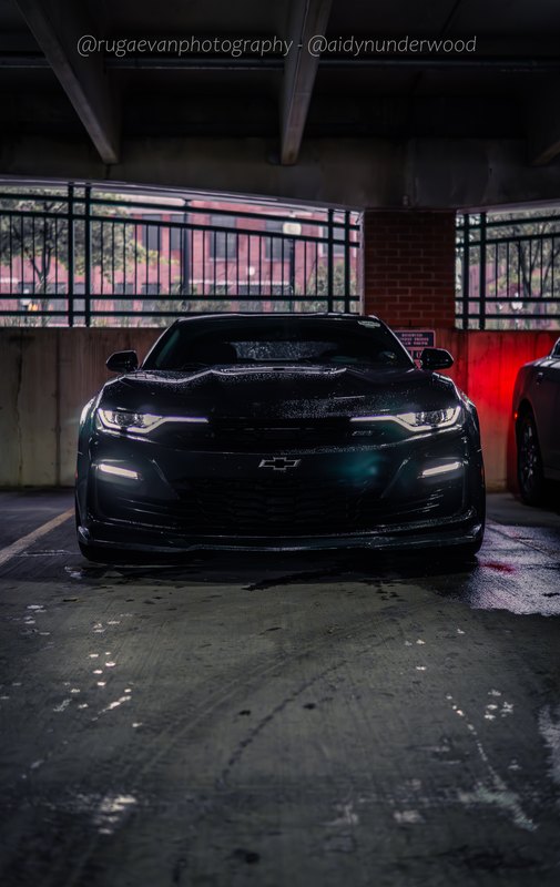 Dark muscle car in a concrete parking garage at night