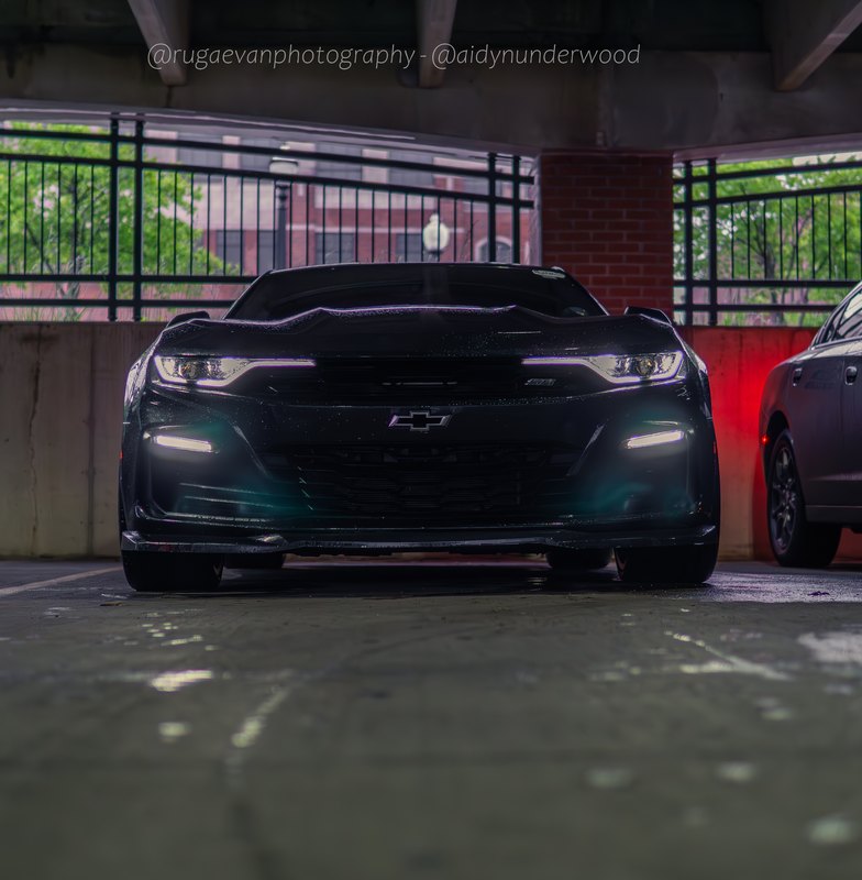 Dark muscle car in a concrete parking garage with red accent light