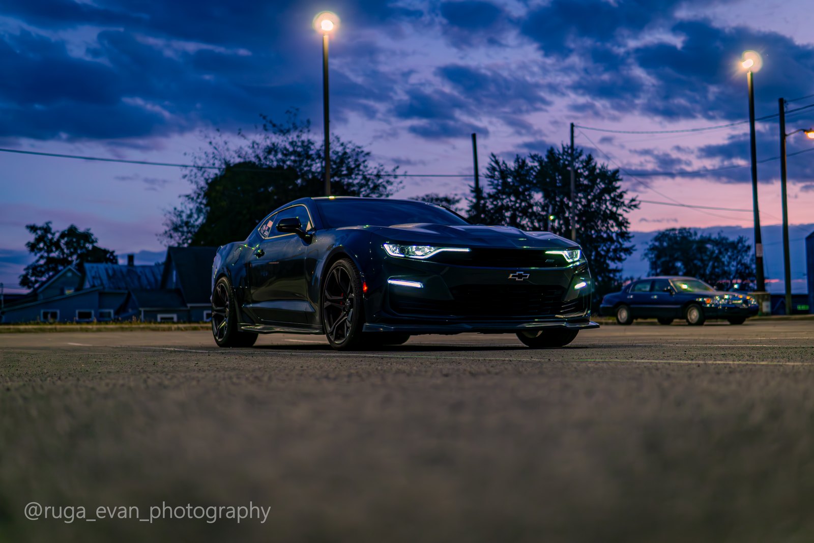 Black Camaro from ground level at blue hour, two streetlights framing it