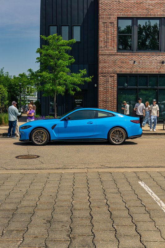 Blue BMW coupe in side profile on a brick-paved street