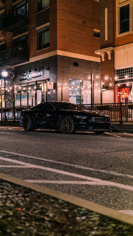 Black Mustang and Camaro on a lit downtown street at night
